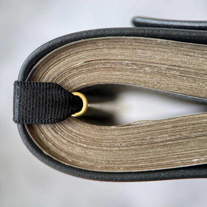 Close-up of a book with a black strap tied around it on a light gray background