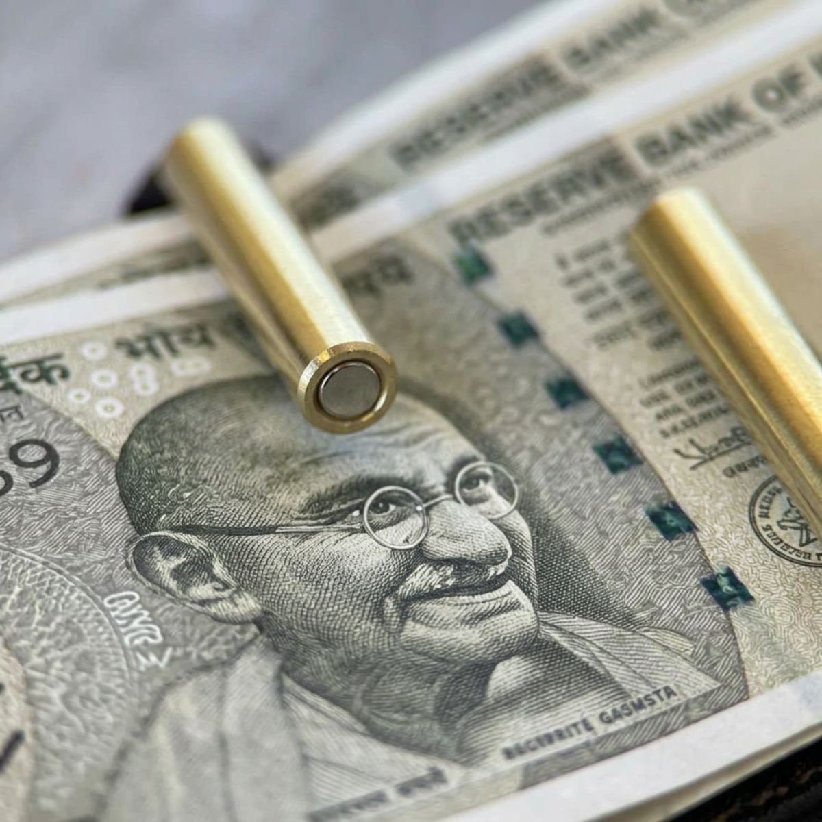 Two gold bullets on top of Indian currency notes with a portrait of a famous person.