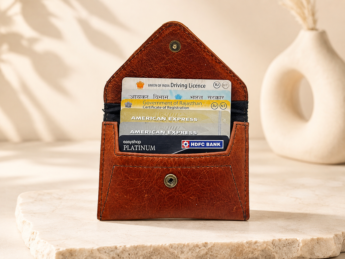 A brown leather card holder wallet standing upright on a stone slab, holding two cards, with a neutral beige background and a decorative vase in the distance.