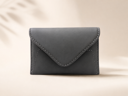 A dark gray envelope-style card holder or small wallet with visible stitching, centered on a warm beige background with soft leaf shadows.