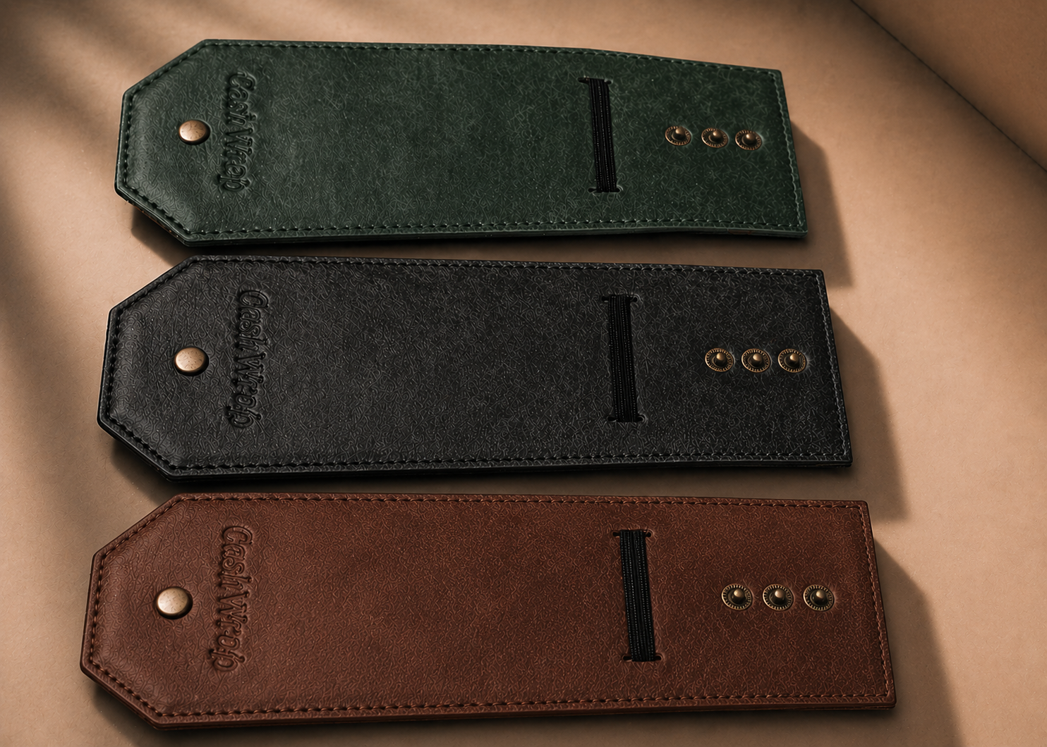 Three leather card sleeves or wallet tabs in dark green, charcoal gray, and brown, arranged vertically on a beige background. Each piece features a snap button closure, a central slot, and brass hardware.