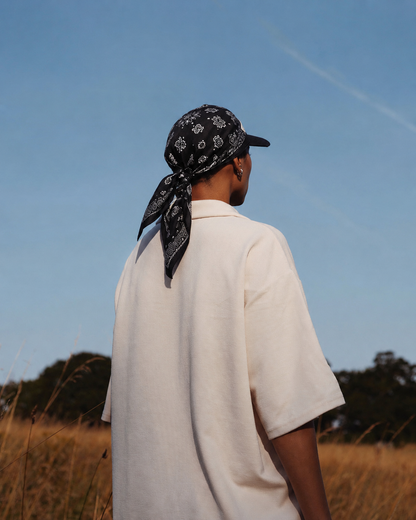 Person wearing a bandana and white shirt standing in a field with a clear blue sky.