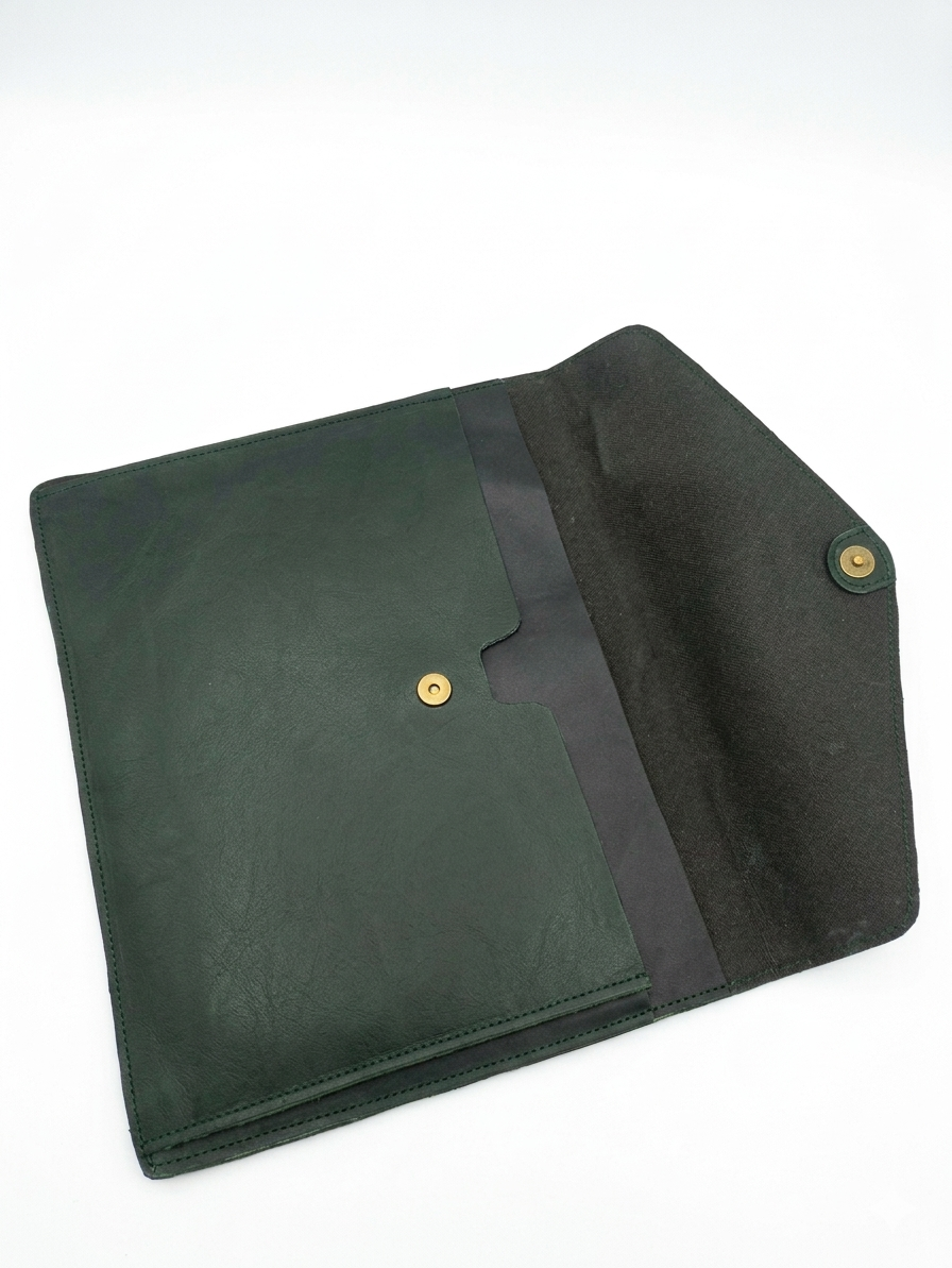 A dark green leather sleeve or clutch with a black fabric interior lining and gold-tone snap buttons, shown open on a white background.