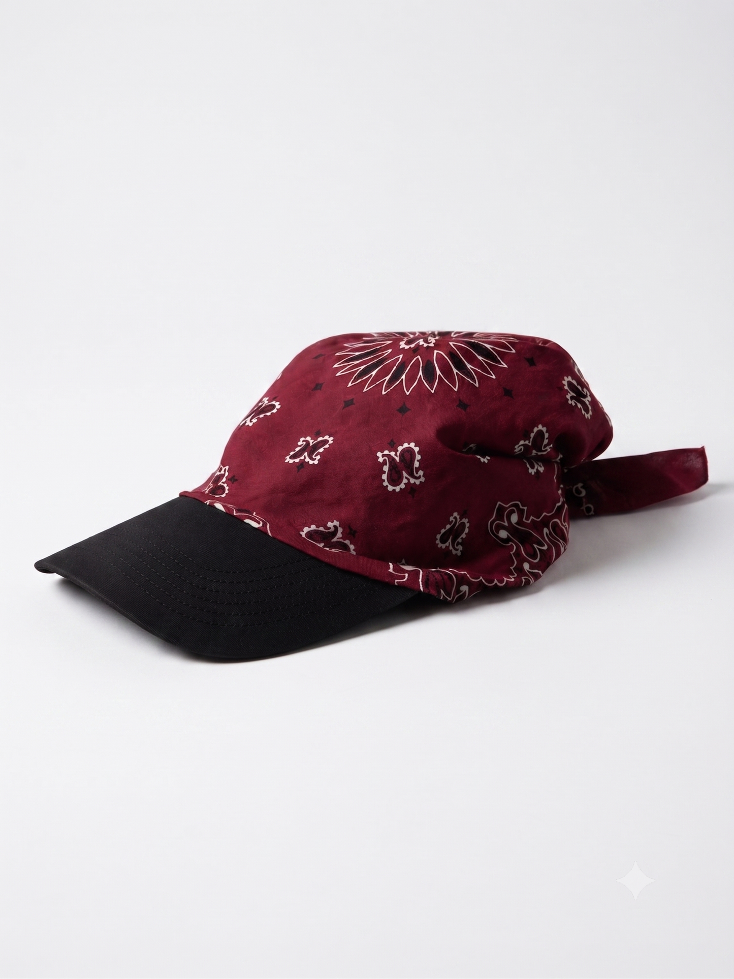 A baseball cap featuring a burgundy bandana print crown and a solid black curved brim, photographed on a clean white studio background.