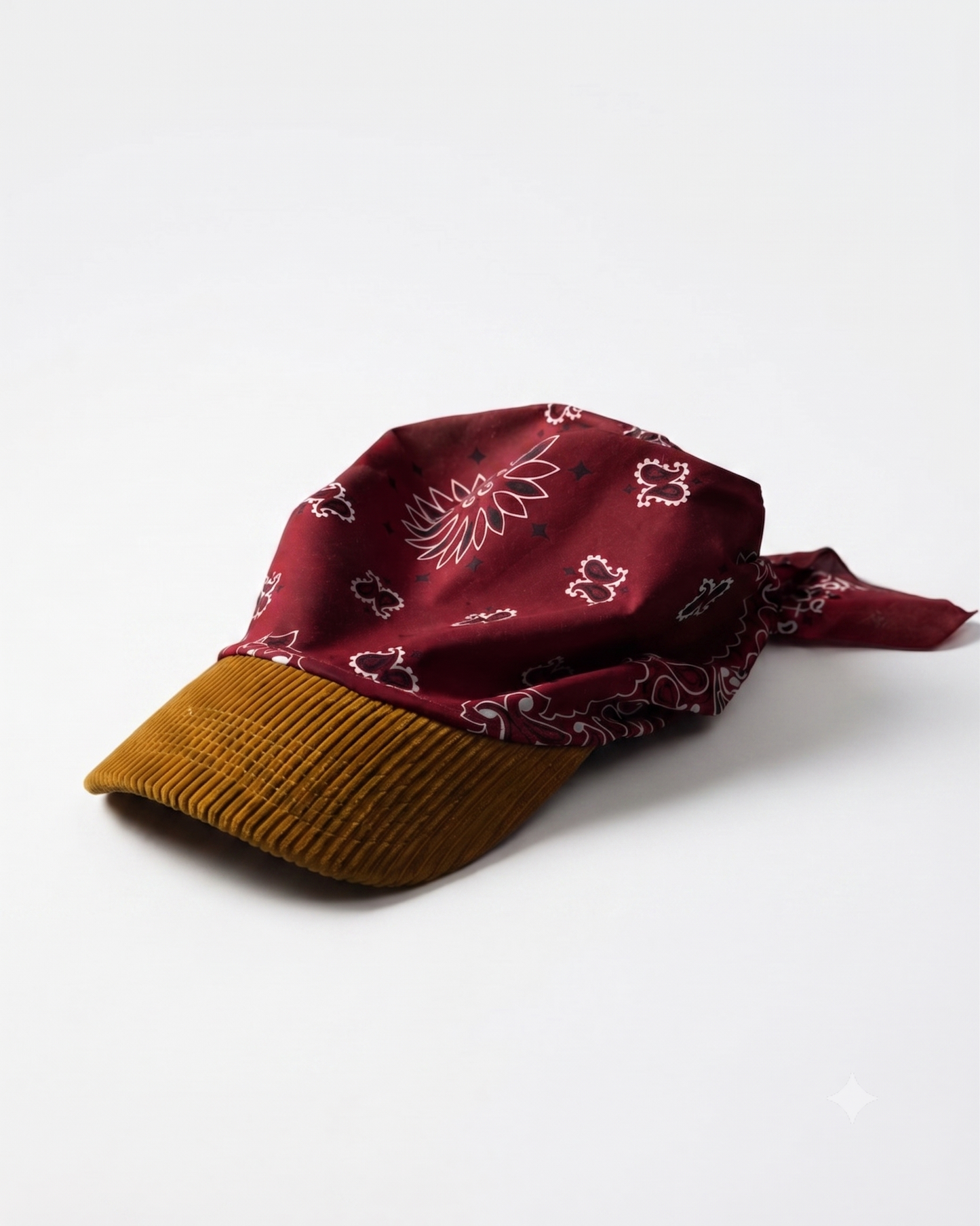 A baseball cap featuring a burgundy silk bandana with a white floral print on the crown and a mustard brown corduroy brim, photographed on a clean white background.