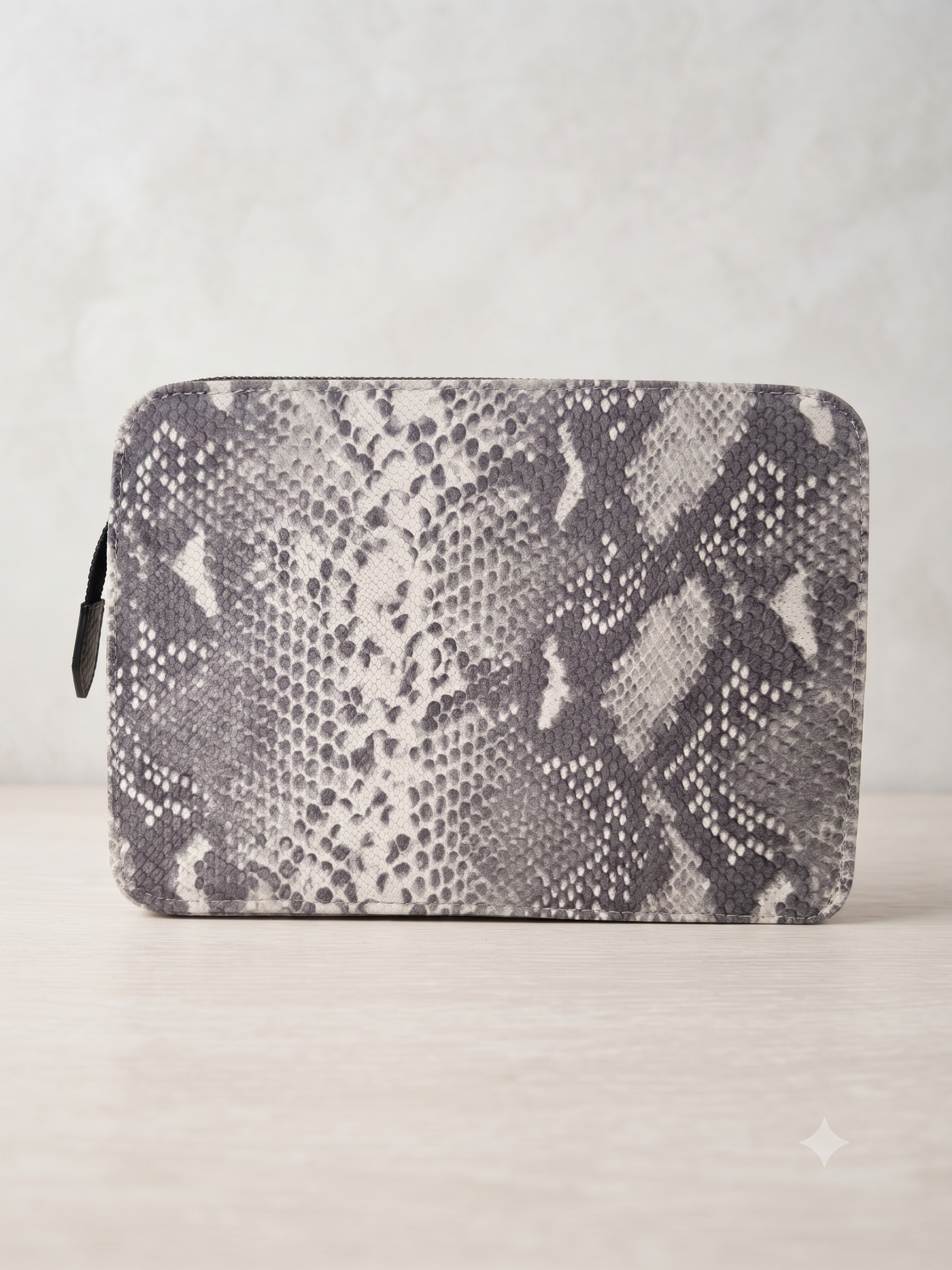 A zippered pouch featuring a gray and white snakeskin pattern, displayed on a light beige surface against a neutral gray background.