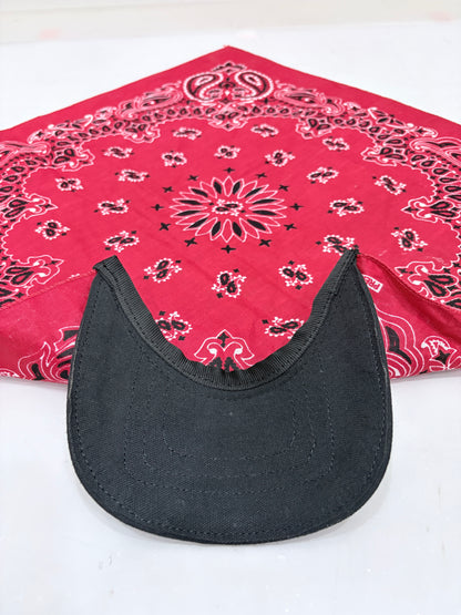 A black curved visor or hat brim placed in front of a folded red bandana with black paisley-style patterns on a white surface.