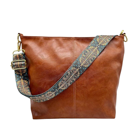 A brown faux-leather hobo-style shoulder bag with a wide, patterned woven strap in blue, beige, and gold tones, and gold-tone hardware, shown on a plain white background.